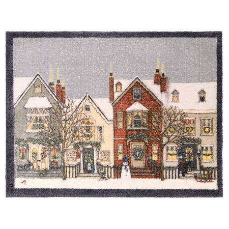 A rectangular doormat featuring a winter village scene with snow-covered houses, bare trees, storefronts, and a gray sky, finished with a dark border.