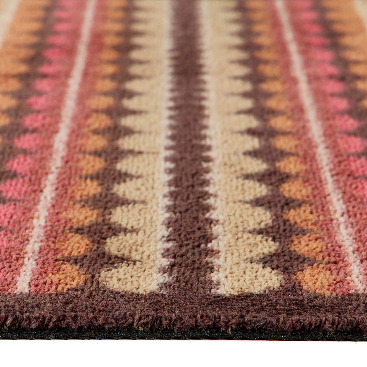 A close-up of a doormat with a Southwestern geometric pattern in brown, beige, pink, and orange, showing the textured pile and fringe edge.
