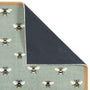A close-up of a rug corner with the top-left section folded back to show the backing. The visible top surface has a pale sage green base with a repeating pattern of bumblebees in black, yellow, and white.