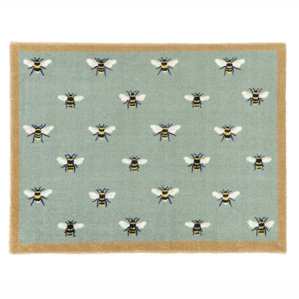 A rectangular area rug with a sage green background featuring a repeating pattern of bumblebees, finished with a natural coloured border.