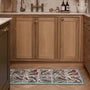 A rectangular kitchen runner with a detailed bird pattern and turquoise border, placed on a herringbone wood floor in front of light oak kitchen cabinets.