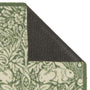 Close-up of a folded outdoor doormat showing a green and cream floral pattern on the top and side, with a dark charcoal backing visible on the underside against a white background.