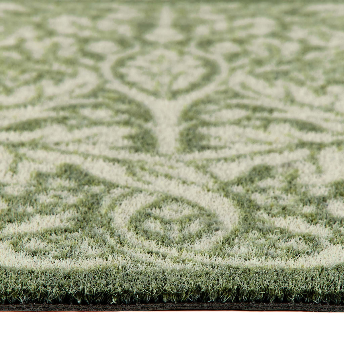 Close-up of a outdoor doromat  with a green and cream damask pattern, showing the pile height and the edge of the doormat. 