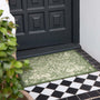 A rectangular outdoor doormat with an ornate green and beige damask pattern, placed on a tiled porch step in front of a black front door.
