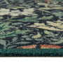 Close-up of a floral outdoor doormat with a dark green, black, and beige abstract floral pattern and a solid dark green shag border.