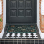 A rectangular floral outdoor doormat in dark green with orange and cream botanical patterns, placed on a tiled entryway in front of a black front door.