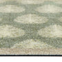 Close-up of a textured doormat with a leaf pattern in sage green, beige, and cream, showing the pile texture and fringed edge.