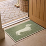 A rectangular green doormat with a white dachshund silhouette, placed in front of an open wooden door on a tiled floor.