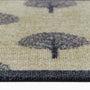 Close-up of a textured doormat with a repeating tree pattern in dark charcoal gray on a warm beige background.