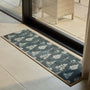 A rectangular runner with a dark green background and a repeating white leaf pattern, placed on a light stone tile floor in front of a glass sliding door.