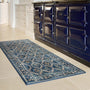 A rectangular blue area rug with a traditional floral and geometric pattern, shown on a light beige tiled kitchen floor next to a glossy black Aga stove.