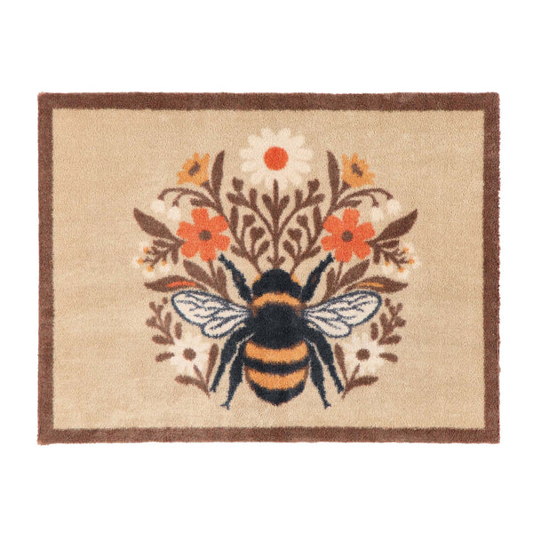 A rectangular doormat with a natural beige background, a dark brown border, and a central bumblebee motif surrounded by orange, white, and yellow flowers.
