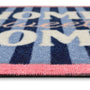 A close-up of a textured doormat featuring navy blue and light blue vertical stripes, cream lettering that reads 'HOME sweet HOME', and a pink border.