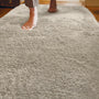 A close-up of a light beige shag rug with a person's bare feet stepping onto it in a home setting.