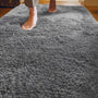 A close-up of a dark gray shag rug with bare feet stepping onto it in a home setting.