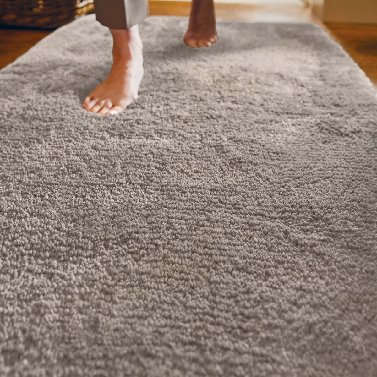 A close-up of a person's bare feet stepping onto a thick, high-pile stone shag rug in a home setting.
