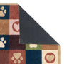 A close-up of a multicolor dog-themed doormat with a checkered pattern of paw prints, hearts, and paw pads in blue, brown, beige, and green, with the underside showing a dark gray textured non-slip backing.