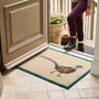 A rectangular entryway doormat with a pheasant illustration and teal border, shown on a tiled floor at a doorway with a person standing outside.