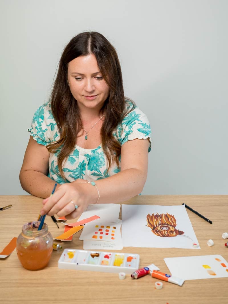 Woman painting a watercolour highland cow for Hug Rug doormats