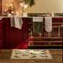A kitchen scene with a beige doormat featuring a robin pattern in the foreground, with matching patterned towels and oven mitts hanging on a red stove and cabinets.