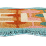 A close-up of a coir doormat with a retro geometric pattern in orange, beige, pink, and teal, featuring a light blue fringe along the bottom edge.