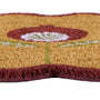 A close-up of a textured coir doormat with a stylized flower design in rust red, light green, and white, featuring a fringed edge on a white background.