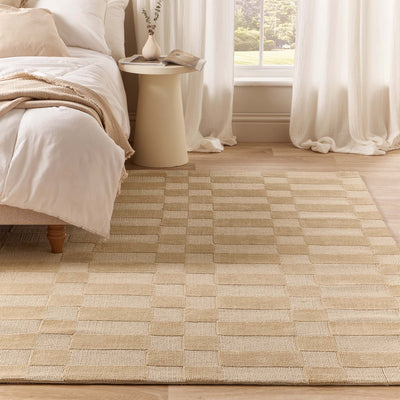 A beige and cream checkered woven area rug styled in a bright, modern bedroom next to a bed and a small side table.