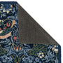 Close-up of a patterned outdoor doormat with the top-left section folded back to show the dark gray backing, on a white background.