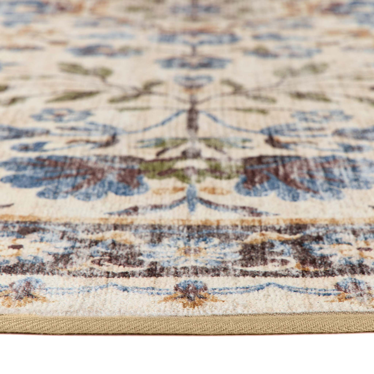 A close-up of a traditional patterned area rug showing its cream base, blue floral motifs, and brown and green accents, with a beige woven border.