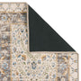 A close-up of a patterned area rug with one corner folded back to show the dark backing, on a plain white background.