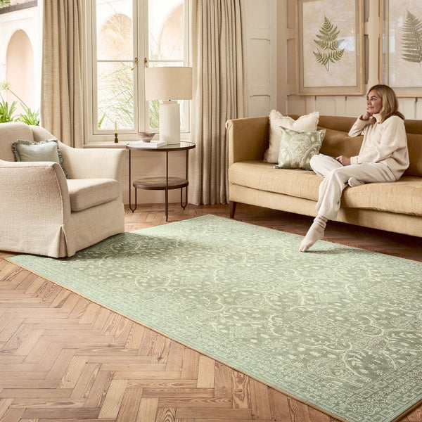 Sanderson By Highgrove x Hug Rug Eco-Washable Topiary View Thyme Rug in green with a traditional style pattern, styled in a living room. 
