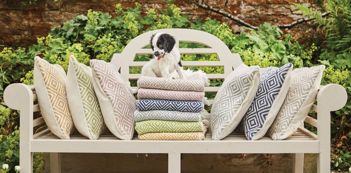 Dog sat on top of Hug Rug woven throws and cushions outside 