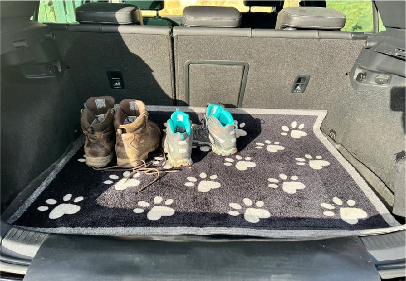 Muddy boots in car boot on top of a paw print design car boot protector