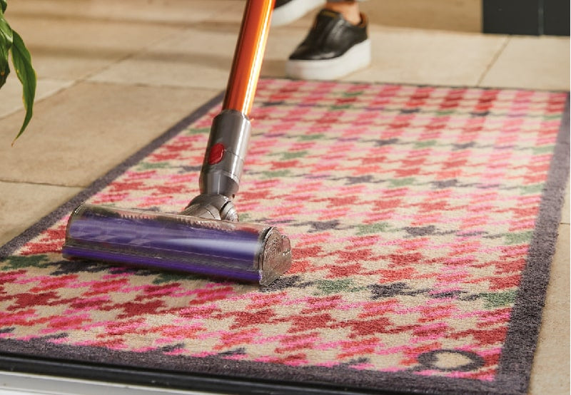 A vaccum hoovering a multicoloured hug rug doormat