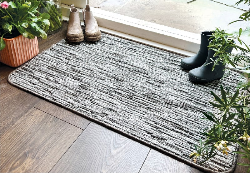 A grey striped utility doormat at the front door with muddy wellies on top