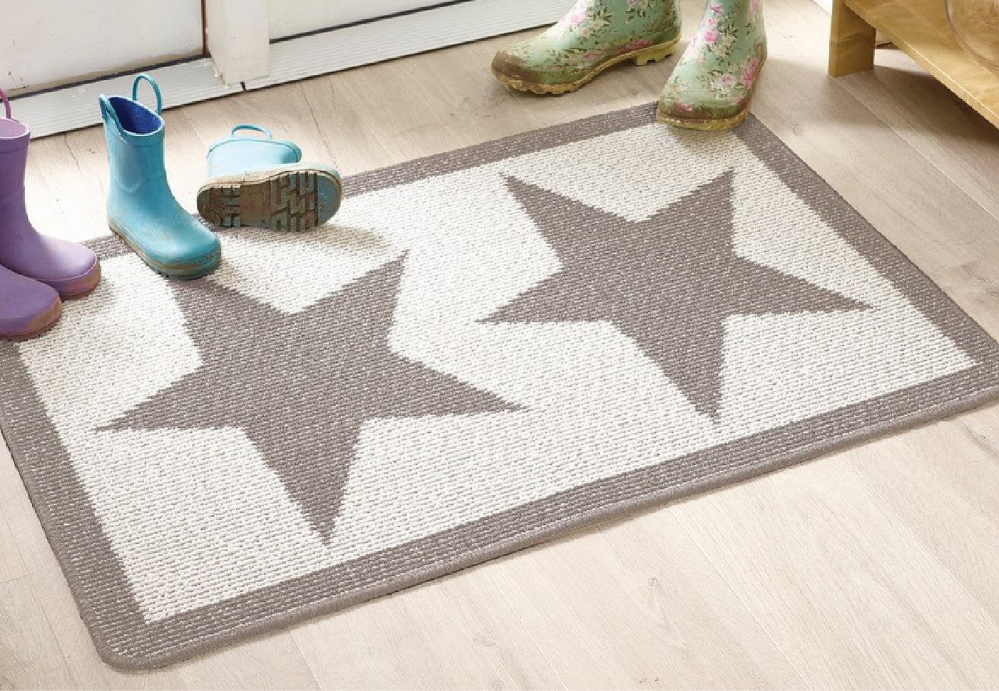 A white front door doormat with 2 grey stars on it surrounded by muddy wellies