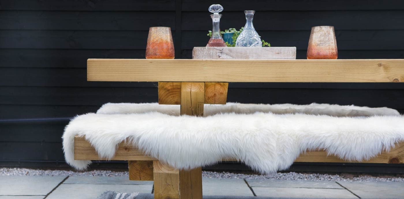 A white sheepskin rug on a wooden bench outside, manufactured by Phoenox Textiles