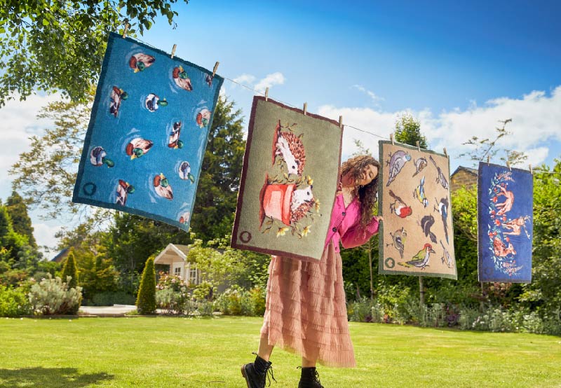 woman holding two nature themed doormats on a washing line outside