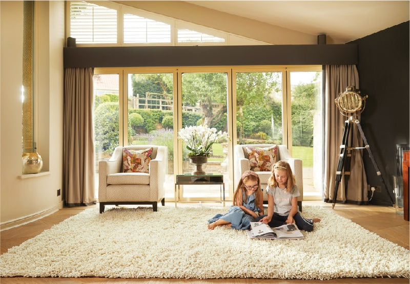 two young girls sat on a large white shaggy rug in a living room