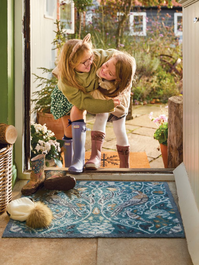 Two little girls standing on a hug rug at the front door of a house.