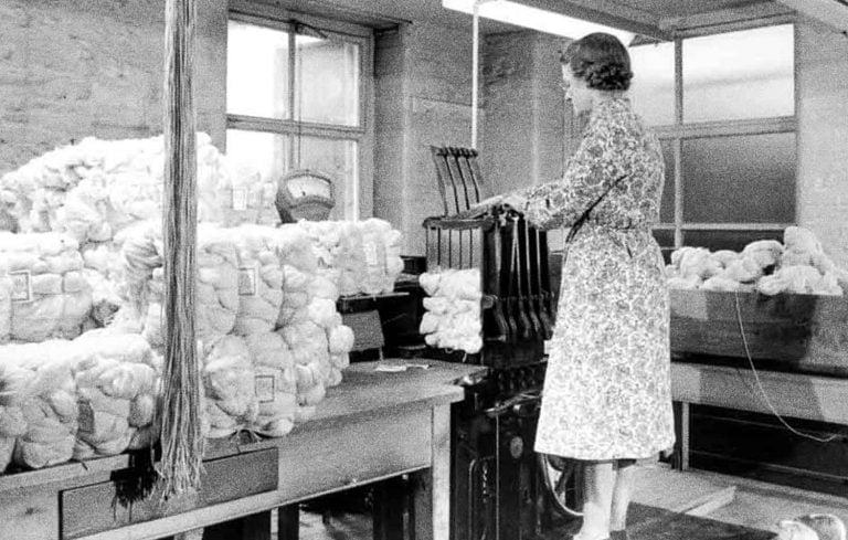a woman standing in a room filled with lots of bags of wool.