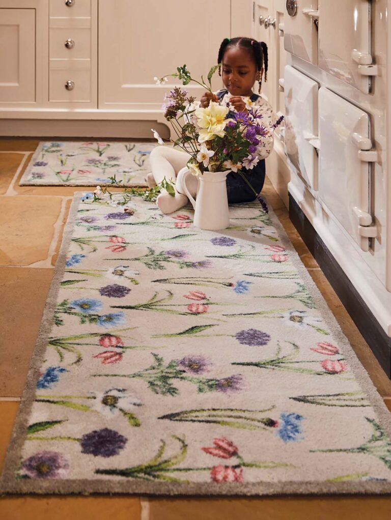 Young girl sat on a rug on the kitchen floor with a vase of flowers