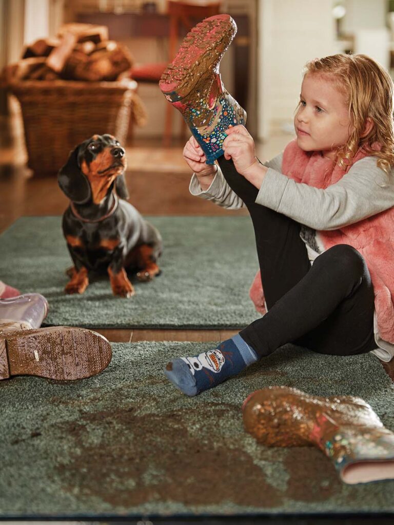 little girl putting here muddy boots on the rug